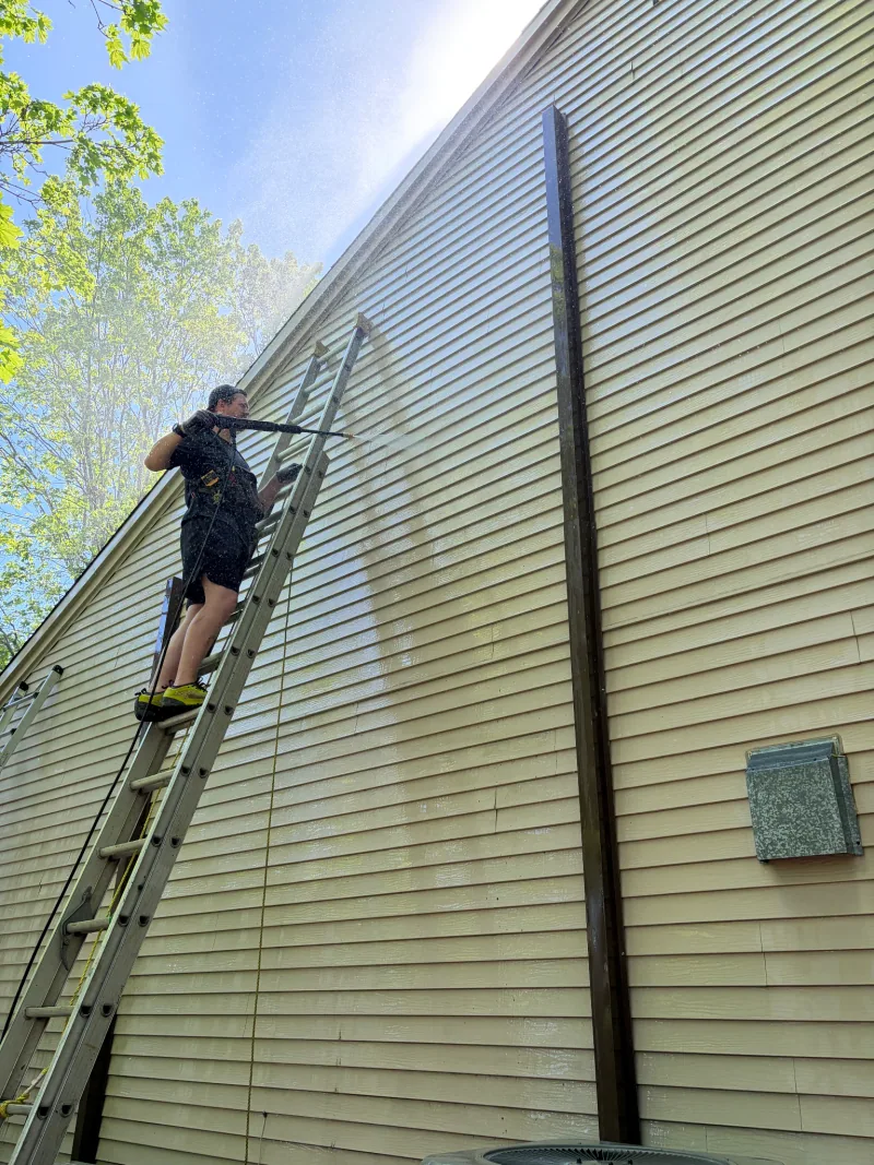 An EDMTL team member cleaning the siding of a home from a ladder.