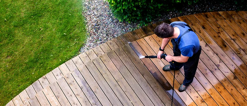 A technician pressure washing a wood deck at a residential property.